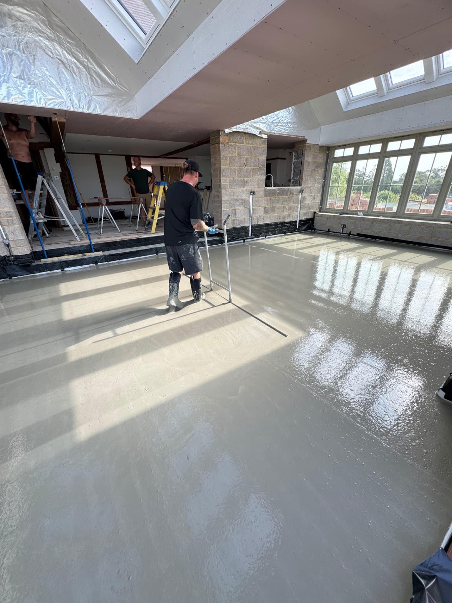 Installer levelling wet liquid screed in a bright house extension